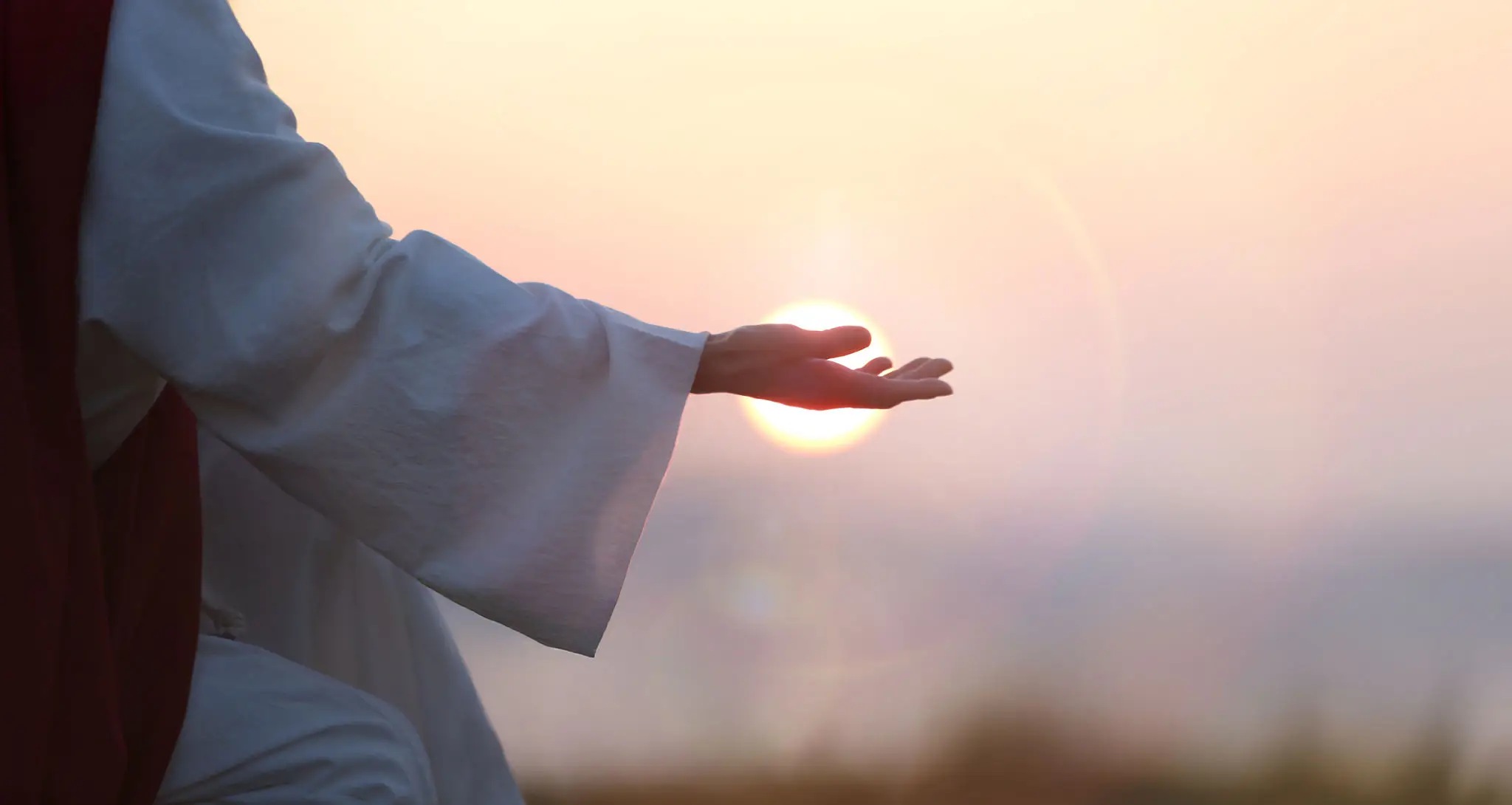 Hand reaching out to a glowing light during sunset.