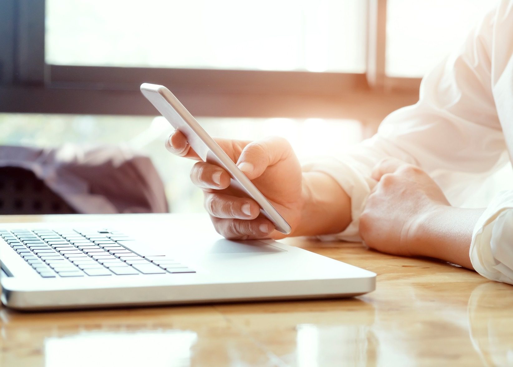 Person using smartphone and laptop at desk