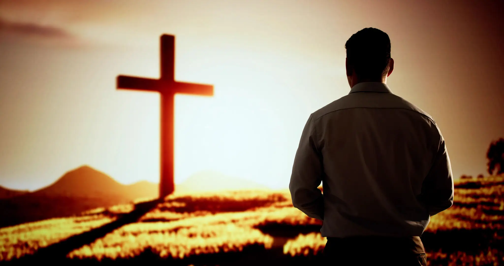 A man standing near a cross at sunset, reflecting in solitude.